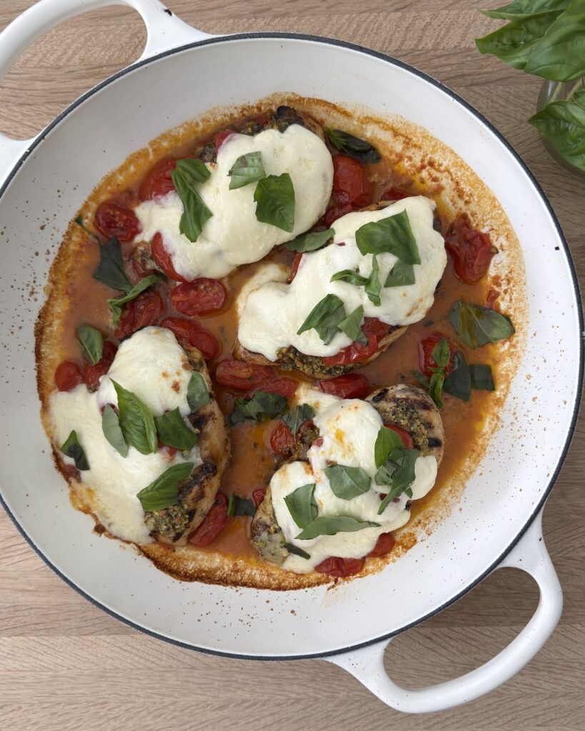 Chicken Margherita with melted mozzarella, blistered tomatoes, basil, and grilled chicken in a white skillet.