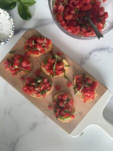 Bruschetta al Pomodoro made with toasted baguette topped with fresh diced tomatoes, basil, olive oil, and flaky sea salt on a wooden serving board.