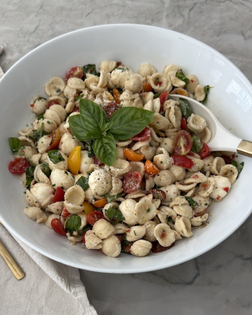 Caprese pasta salad with orecchiette, fresh mozzarella, cherry tomatoes, basil, and balsamic vinaigrette in a white serving bowl.