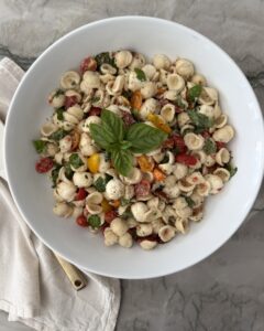 Caprese pasta salad with orecchiette, fresh mozzarella, cherry tomatoes, basil, and balsamic vinaigrette in a white serving bowl.
