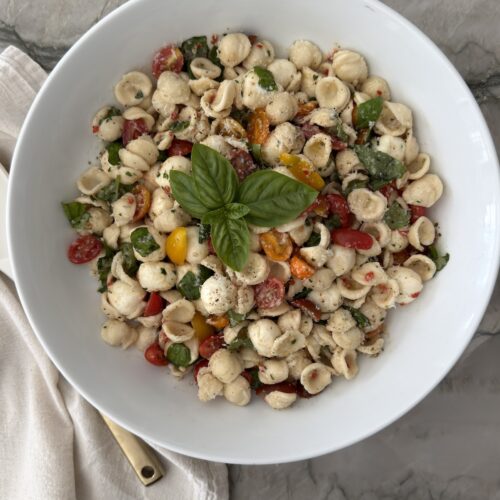 Caprese pasta salad with orecchiette, fresh mozzarella, cherry tomatoes, basil, and balsamic vinaigrette in a white serving bowl.