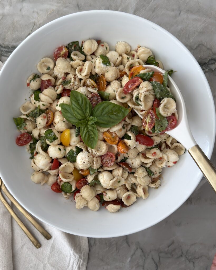 Caprese pasta salad with orecchiette, fresh mozzarella, cherry tomatoes, basil, and balsamic vinaigrette in a white serving bowl.