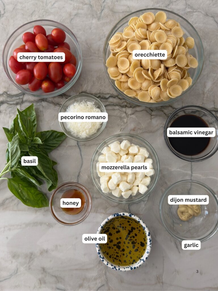 Ingredients for Caprese pasta salad including orecchiette pasta, cherry tomatoes, mozzarella pearls, fresh basil, Pecorino Romano, balsamic vinegar, Dijon mustard, and honey.