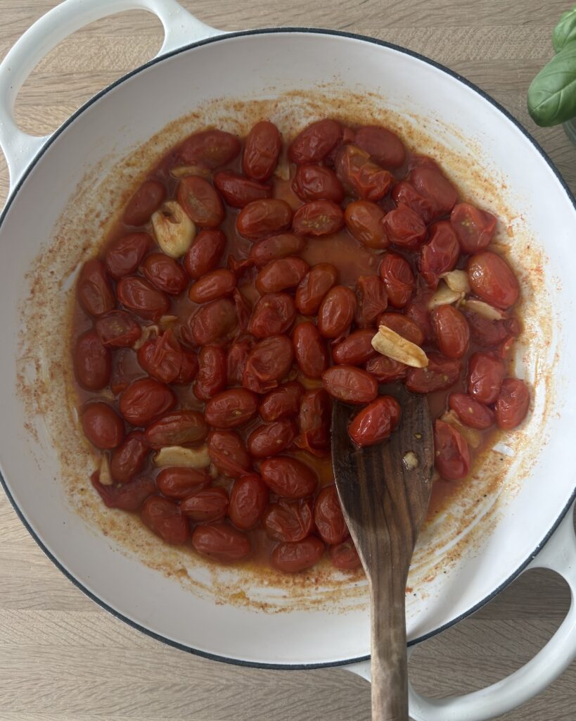 Cherry tomatoes and garlic simmering in a skillet before blending into a creamy tomato pasta sauce.