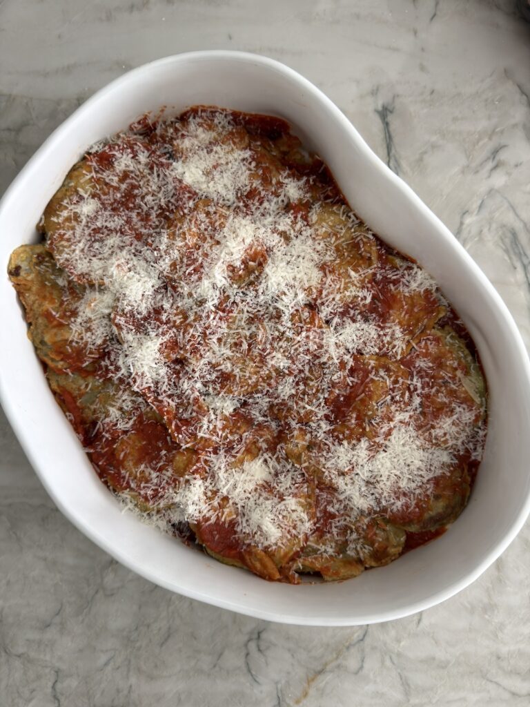 Baked eggplant Parmesan topped with marinara, melted mozzarella, and grated Parmesan in a white oval baking dish.
