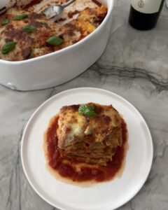 A serving of eggplant Parmesan with golden melted mozzarella and fresh basil over marinara sauce on a white plate.