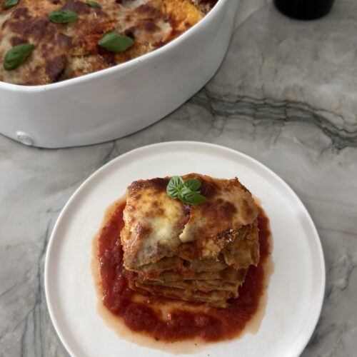 A serving of eggplant Parmesan with golden melted mozzarella and fresh basil over marinara sauce on a white plate.