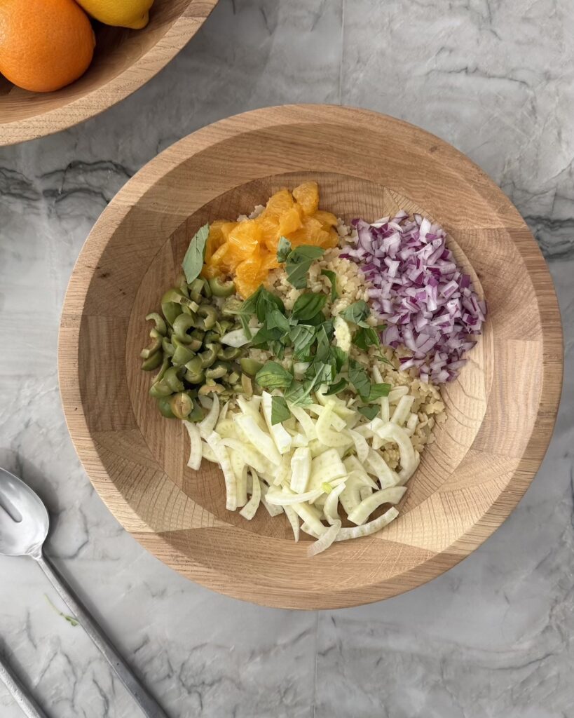 Pastina salad ingredients with fennel, orange, red onion, basil, olives, and ricotta salata in a wooden bowl