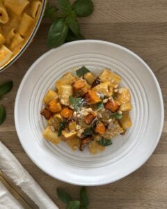 Creamy butternut squash pasta topped with roasted squash cubes, Parmesan, basil, and pine nuts in a white bowl.