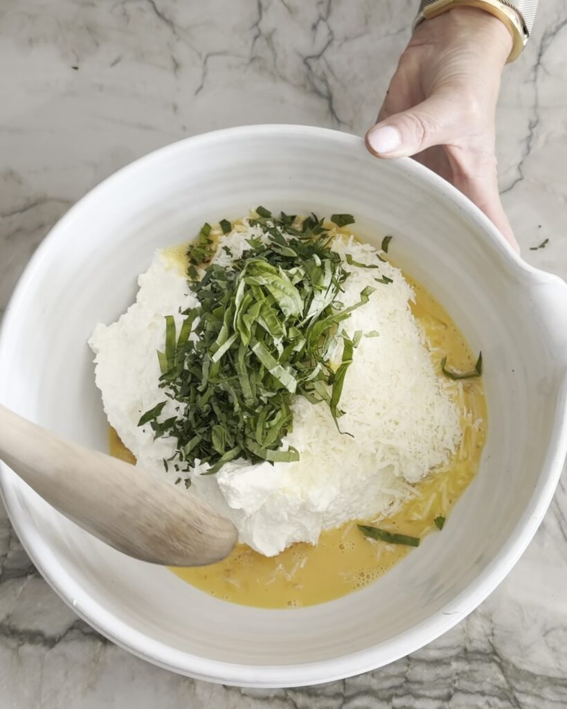 Ricotta, eggs, grated Parmesan cheese, and chopped fresh basil in a mixing bowl for homemade lasagna filling